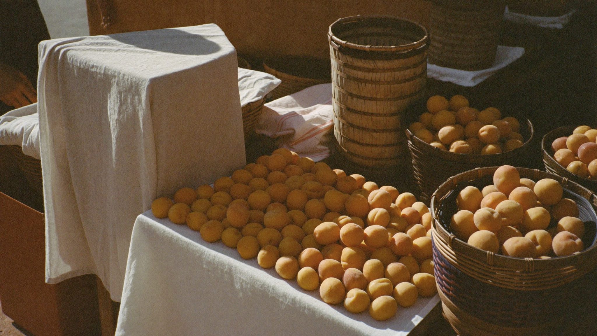 Étal de marché provençal, linge et fruits sous une lumière dorée